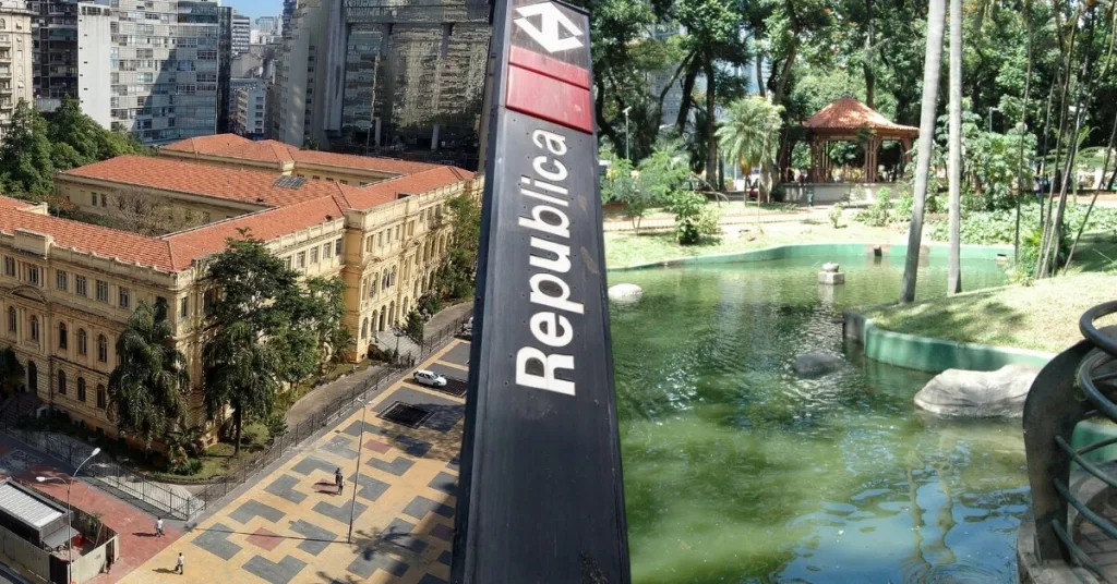 Placa da Estação República do metrô em primeiro plano, com detalhes da Praça da República, tendo a Escola Caetano de Campos de um lado e o lago e coreto da praça do outro lado no centro de São Paulo.
